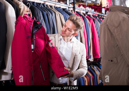 Homme ordinaire de l'examen du client dans les manteaux magasin vêtements Banque D'Images