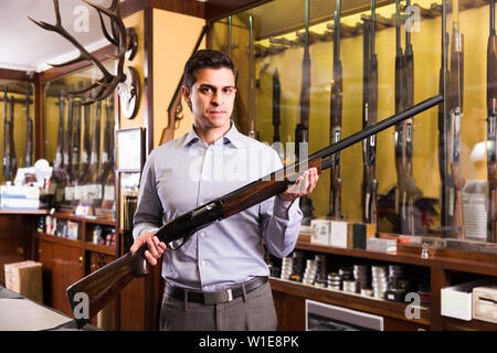 Brunette homme hunter choisissant fusil en magasin avec l'équipement de recherche de Banque D'Images