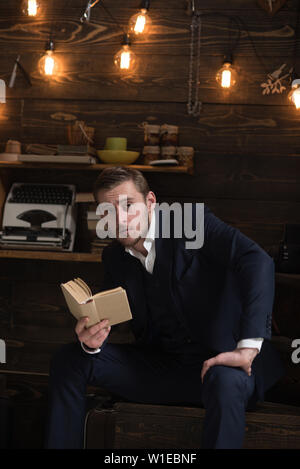 Profitez de moment. Homme à barbe est titulaire d'ancien livre et le lire. Guy en atmosphère chaude agréable lors de la lecture de détente. L'homme en costume officiel profitez de soirée avec faveur Banque D'Images