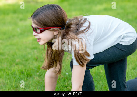 Une fille sportive enfant portant des lunettes ou des lunettes de sport sur ordonnance participant à l'athlétisme - sprint start Crouch Banque D'Images