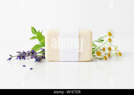 Gros plan du savon à base de plantes fait main bar dans le papier vierge paquet d'étiquettes. Les feuilles de menthe, de lavande et de camomille fleurs sur fond de table blanc. Spa concept Banque D'Images