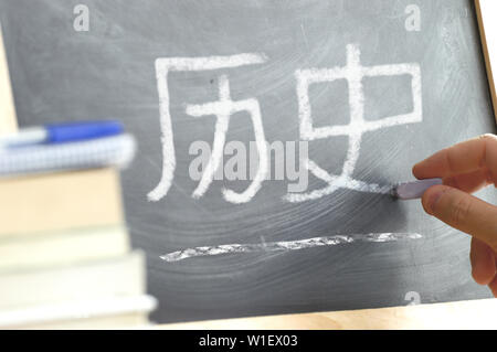 La main sur un tableau noir dans l'histoire chinoise classe avec le mot écrit sur l'histoire. Des livres et du matériel scolaire. Banque D'Images