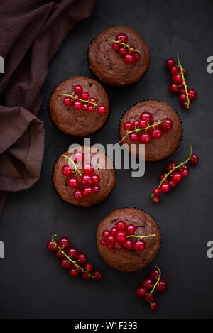 Vue de dessus sur muffins au chocolat décoré de petits fruits groseille rouge foncé sur fond de bois. Mise à plat. Soft focus Banque D'Images