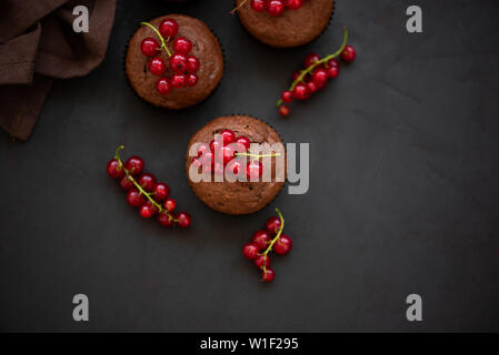 Vue de dessus sur muffins au chocolat décoré de petits fruits groseille rouge foncé sur fond de bois. Mise à plat. Soft focus Banque D'Images