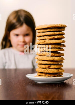 Photo d'une jeune fille devant un grand tas de cookies aux pépites de chocolat. Se concentrer sur les cookies. Banque D'Images