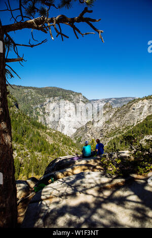 Touristes randonneurs assis au bord d'une falaise à l'ombre d'un arbre dans John Muir Trail, en été avec un ciel bleu clair, le parc national de Yosemite Banque D'Images