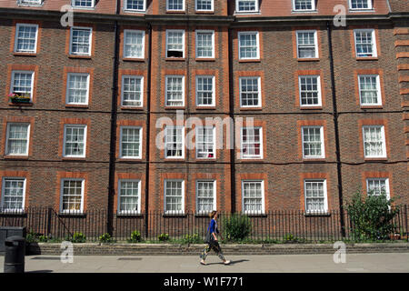 Une femme passe l'extérieur d'un bâtiment faisant partie de l'Hammersmith 1926 estate, propriété de la peabody trust, Hammersmith, Londres, Angleterre Banque D'Images
