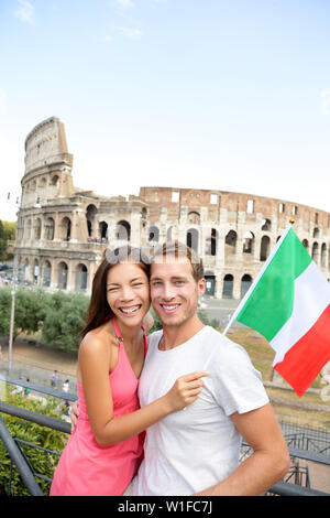 En toute sécurité avec une assurance voyage - couple de touristes devant le Colisée, Rome, Italie. Cheerful Young Asian and Caucasian adultes posant avec drapeau italien au cours de leurs vacances en Europe vacances en Europe. Banque D'Images