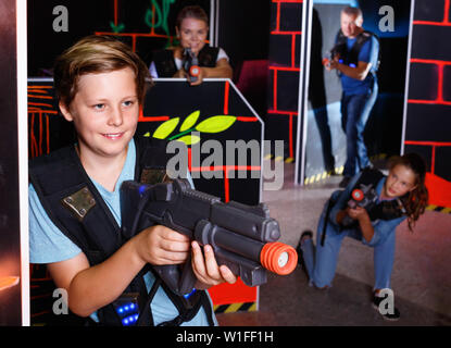 Heureux happy smiling boy positives visant pistolet laser à d'autres joueurs pendant le jeu laser tag in dark room Banque D'Images