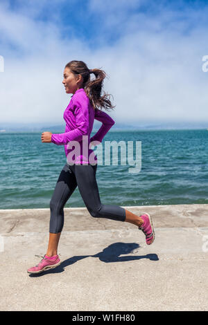 Woman running on port au bord de l'embarcadère de San Francisco, Californie, USA. Mixed Race fit fitness sport modèle dans Printemps / Automne vêtements en tenue. Smiling happy runner de l'athlète féminine de la formation. Banque D'Images