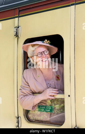 Kidderminster, Royaume-Uni. 29 juin 2019. Severn Valley Railways, qui remonte aux années 1940, a pris un fabuleux départ cet été avec des réacteurs qui jouent leur rôle dans une authentique reconstitution de la Grande-Bretagne de la Seconde Guerre mondiale. Une femme d'âge moyen souriante isolée, dans les années 1940, est penchée hors de la calèche d'époque, regardant par la fenêtre du train à vapeur alors que le train part de la gare du patrimoine. Crédit: Lee Hudson Banque D'Images