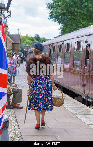 Kidderminster, Royaume-Uni. 29 juin 2019. Les chemins de fer de Severn Valley « revenez aux années 1940 » débutent cet été avec des réacteurs qui jouent leur rôle pour offrir une authentique récréation de temps de guerre, la seconde Guerre mondiale. Une femme de la mode des années 1940, capturée par derrière, descend la plate-forme ferroviaire du patrimoine pour monter à bord en attendant le train à vapeur vintage. Crédit: Lee Hudson Banque D'Images