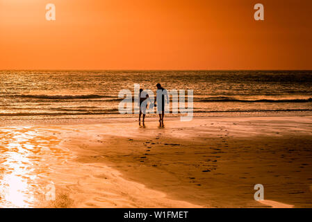 Les gens vu en silhouette comme un beau coucher du soleil se couche sur la plage de Fistral à Newquay en Cornouailles. Banque D'Images