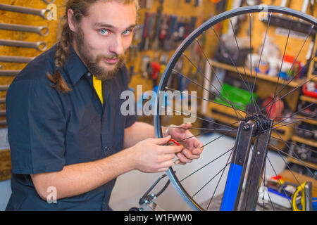 Blue Eyed beraded guy en chemise noire la réparation de bicyclette dans l'atelier Banque D'Images