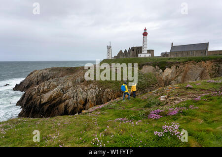 La mère et le fils debout sur clifs par le phare et l'abbaye s'élevant au-dessus de la mer et la côte rocheuse de la Pointe Saint-Mathieu en Bretagne, France Banque D'Images