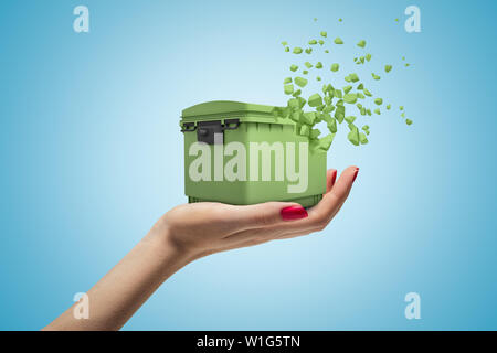 Gros plan du côté de woman's hand holding green à partir de corbeille à se dissoudre en petits morceaux sur fond dégradé bleu clair. Banque D'Images
