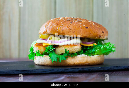 Cheeseburger appétissant avec nuggets de poulet croustillant, cornichon et légumes frais Banque D'Images