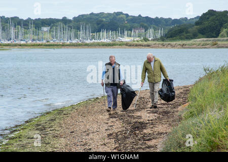 Deux hommes âgés d'effectuer un nettoyage de la plage. Les bénévoles avec des sacs poubelle noirs marchant le long d'une plage de galets. Banque D'Images