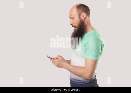 Vue de côté portrait d'homme barbu à tête choquée looking at mobile smart phone afficher avec surpris face. La lecture de bonnes nouvelles ou indo quelque chose d'incroyable. Banque D'Images