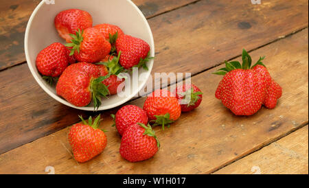 Fraises rouge dans un bol, le bol est sur le côté sur une table en bois rustique et les fraises ont débordé sur la table Banque D'Images