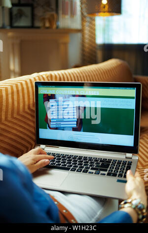 Femme au foyer assis sur le divan dans le salon moderne à sunny chaude journée d'été à l'aide d'apprentissage vidéo site web sur un ordinateur portable. Banque D'Images