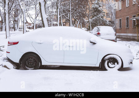 Voiture blanche couverte de neige garée près de la maison. tempête s'endormit car. Banque D'Images