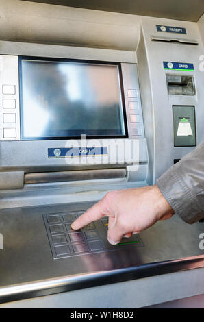 La main d'un homme pousse les touches numériques pour entrer le code pin dans le guichet automatique. Banque D'Images