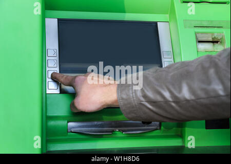 La main d'un homme pousse les touches numériques pour entrer le code pin dans le guichet automatique. Banque D'Images