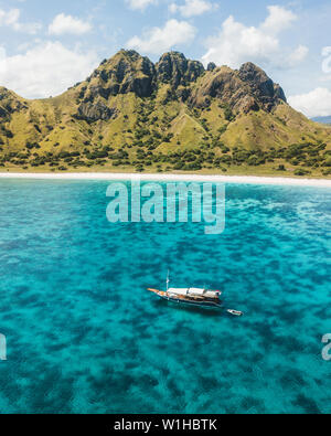 Bateau de croisière naviguant sur les récifs coralliens avec une plage tropicale et sur la montagne. Vue aérienne. L'île de Padar, Komodo en Indonésie. Banque D'Images