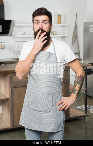 Étant complètement à perte. Surpris cook couvrant sa bouche ouverte avec la main. Homme barbu portant un tablier cuisinier dans la cuisine. Cuire sur son lieu de travail. Aller à cuisiner quelque chose de spécial. Banque D'Images