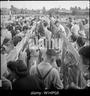 Poston, Arizona. Le bus attend à l'extérieur et les jeunes et vieux ont hâte d'être à l'arrêt. Après la finale pl . . . ; Portée et contenu : la légende complète pour cette photographie se lit comme suit : Poston, Arizona. Le bus attend à l'extérieur et les jeunes et vieux ont hâte d'être à l'arrêt. Après la finale des plans ont été faits, des boîtes emballées, et dons ramassés, les résidents de Poston sont enfin prêts à quitter le centre. Maintenant que beaucoup de leurs amis sont venus avant eux, c'est avec un sentiment d'anticipation plutôt que de tristesse que les évacués se préparer à quitter le lieu que pour les trois dernières années a été la maison pour eux. Banque D'Images