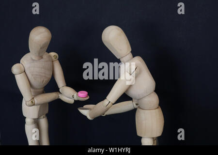 2 mannequins de bois l'un d'accepter une pilule rose tablet médicament de l'autre. La prise de médicaments illégaux décision choix concept. drug education awa Banque D'Images