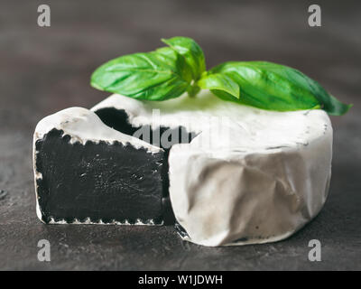 Camembert noir inhabituel avec moisissure blanche.cuisine moderne très tendance,repas,la nourriture.Vue rapprochée du slice noir bio camembert sur fond noir, avec des feuilles de basilic vert.Copy space for text.Banner Banque D'Images