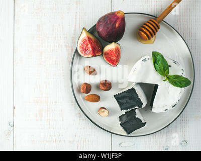 Camembert noir inhabituel avec moisissure blanche.cuisine moderne très tendance,repas,la nourriture.vue du dessus de la plaque,noir,tranches de camembert vert frais basil,figues,écrous,miel sur fond de bois blanc Banque D'Images
