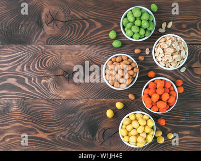 Assortiment de différents arachides snack pour la bière, vin, partie bar. Arachides salées arachides, noix de coco, dans la glaçure verte, rouge piment épicé vasabi, fromage jaune vernis sur table en bois brun. Copier l'espace. Banque D'Images