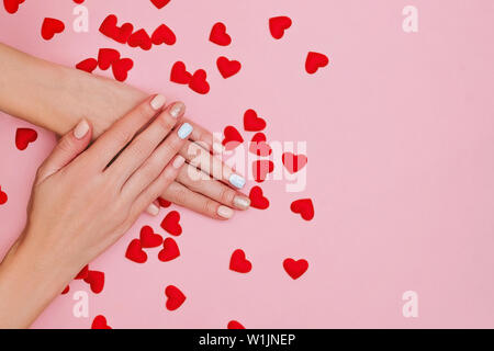 Woman's hands avec manucure pastel sur fond rose avec des coeurs rouges. Concept de la Saint-Valentin. Place pour le texte. Banque D'Images