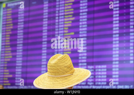 Un homme dans un chapeau de paille est debout devant une commission d'information floue pour les arrivées et départs. Le stand d'information à l'aéroport, à la Banque D'Images