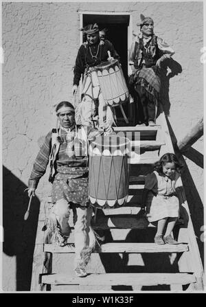 Deux Indiens descendant un escalier en bois, transportant des tambours ; un autre Indien et de l'enfant près de par, danse, San Ildefonso Pueblo, New Mexico, 1942. (Orientation verticale), 1942 Banque D'Images