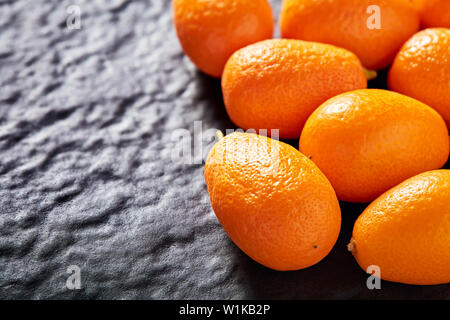 Tas de kumquats sur fond noir pierre texturés avec copie espace. Close up macro-vision. Banque D'Images