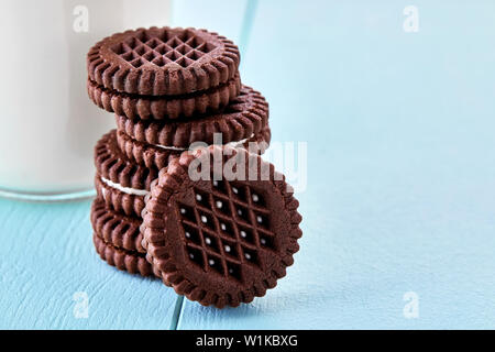 Round biscuits au chocolat rempli de crème glacée et une bouteille de lait sur la table en bois bleu. Macro-vision. Banque D'Images