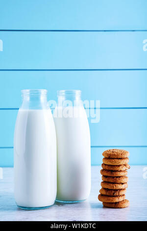 Deux bouteilles de lait et biscuits aux pépites de chocolat sur la table en bois avec fond en bois bleu. Banque D'Images