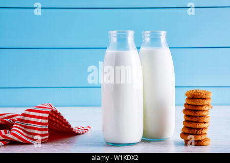 Deux bouteilles de lait et biscuits aux pépites de chocolat sur la table en bois avec fond en bois bleu. Banque D'Images