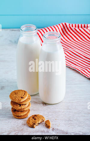 Deux bouteilles de lait et biscuits aux pépites de chocolat sur la table en bois avec fond en bois bleu. Banque D'Images