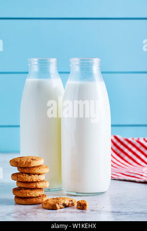 Deux bouteilles de lait et biscuits aux pépites de chocolat sur la table en bois avec fond en bois bleu. Banque D'Images