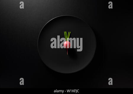 Un navet radis ou servi dans la plaque noire sur fond noir Moody. Vue d'en haut. Régime alimentaire sain concept. Banque D'Images