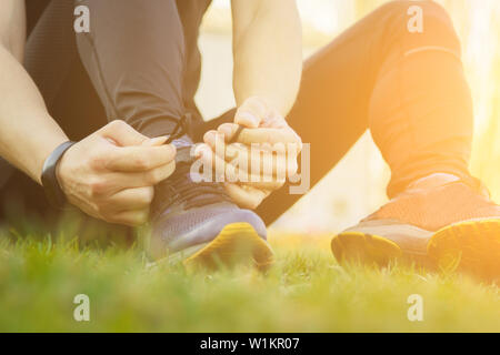 Un jeune homme dans des vêtements noirs est de lier les lacets sur les sneakers close up. fitness sportif assis sur le terrain de sport sur l'herbe. réchauffer prepa corps Banque D'Images