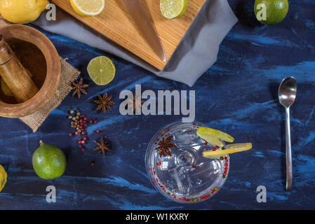 Gin Tonic dans une tasse en verre avec tranches de lime et de citron, le poivre rose et anis sur un fond rustique bleu et noir Banque D'Images