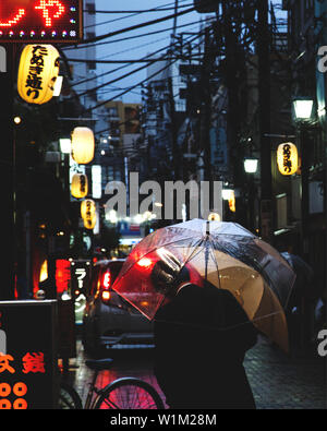 Photo de l'homme avec parapluie debout dans une allée à Tokyo un jour de pluie dans la nuit Banque D'Images