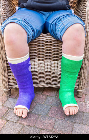 Teenage boy sitting in chair avec deux jambes de gypse de couleur à l'extérieur Banque D'Images