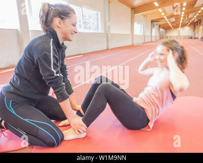 Instructeur de conditionnement physique aider young woman doing sit-ups en athlétisme hall sur piste en tartan, Offenburg, Bade-Wurtemberg, Allemagne Banque D'Images